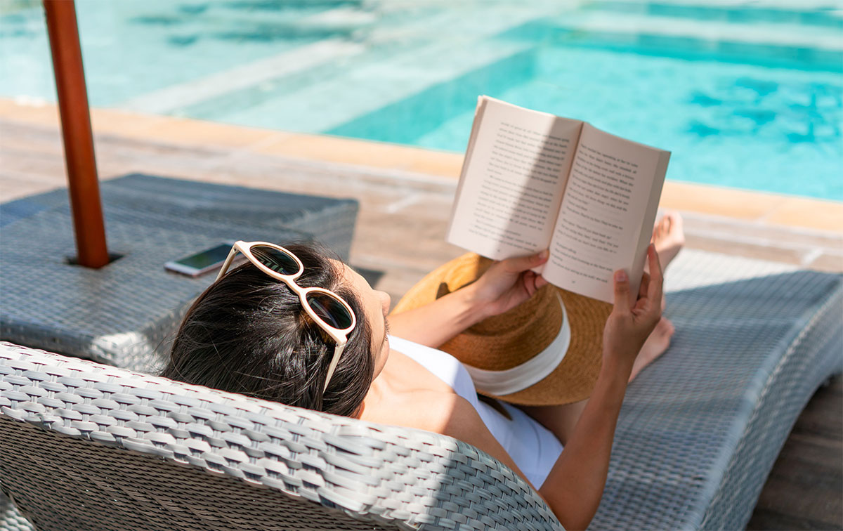 gIRL ON SUNBED ON VACATION READING BOOK BY A POOL